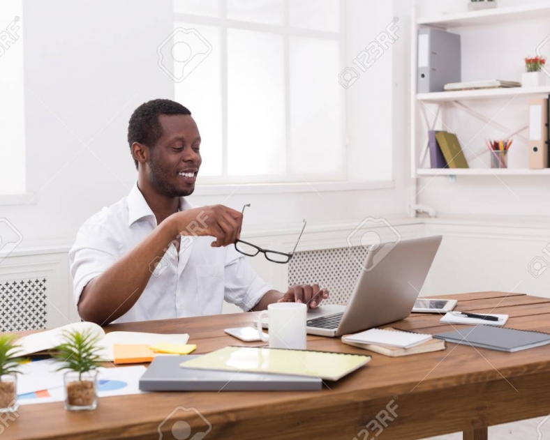 Happy black businessman in office. Successful employee at work with computer. Lifestyle portrait